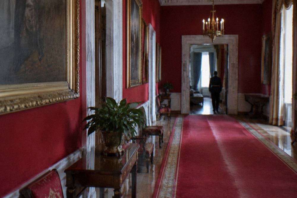 Ornate classical interior hallway with red walls, gilded details, and portrait paintings