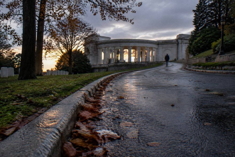 A quiet cemetery roadway curving uphill past trees toward the Memorial Amphitheater at Arlington National Cemetery