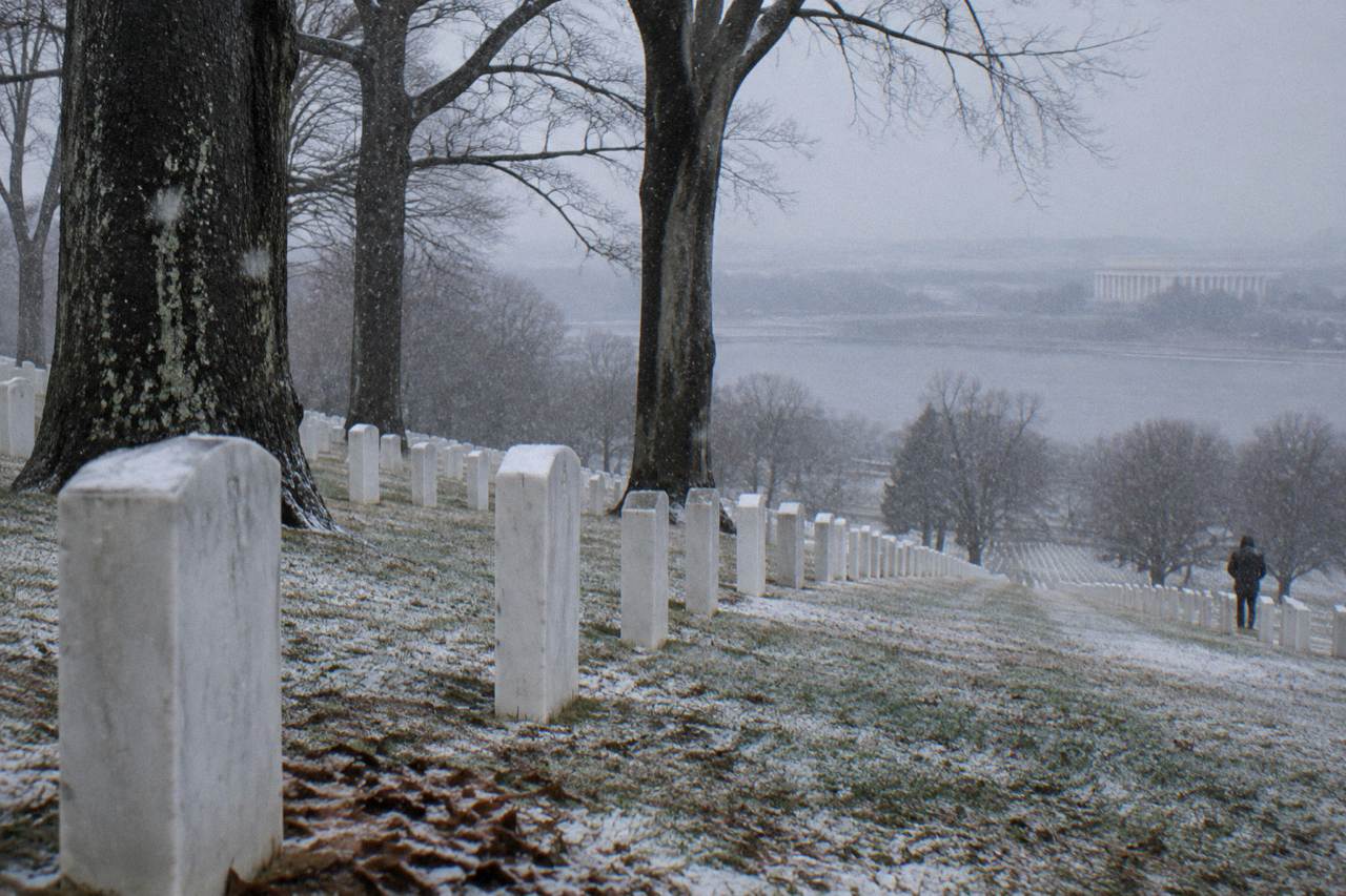 Rows of white headstones on the green hillsides of Arlington National Cemetery with the grounds stretching toward the Potomac River