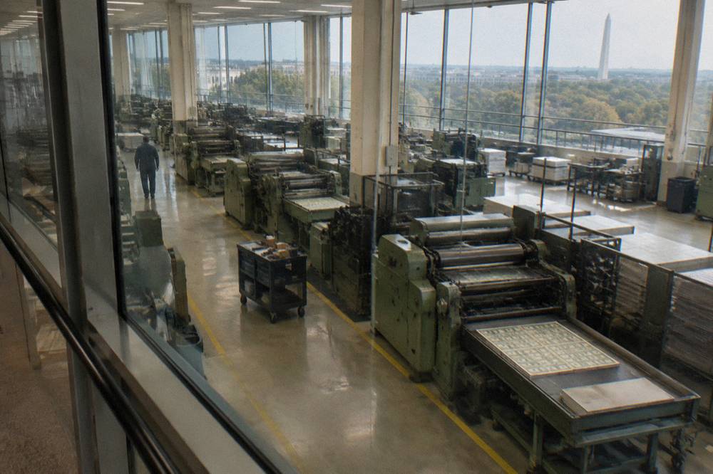 A raised viewing gallery overlooking rows of currency printing presses in a bright production hall