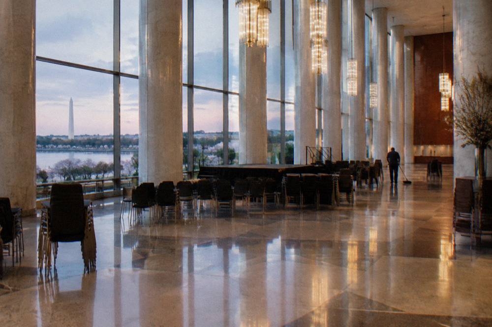 A small stage and rows of empty chairs set up in a grand columned foyer before a free evening performance