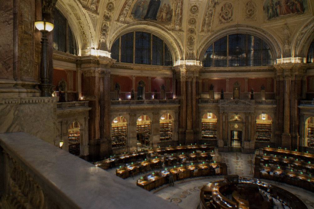 Reading room of the Library of Congress with desks and lamp light under a high domed ceiling