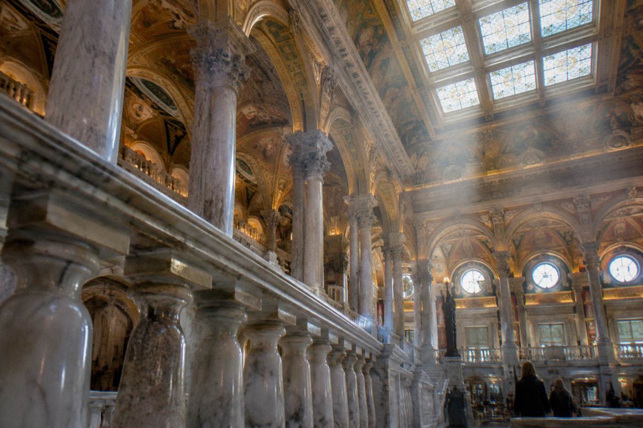 The ornate interior of the Library of Congress Great Hall with marble arches and a painted ceiling