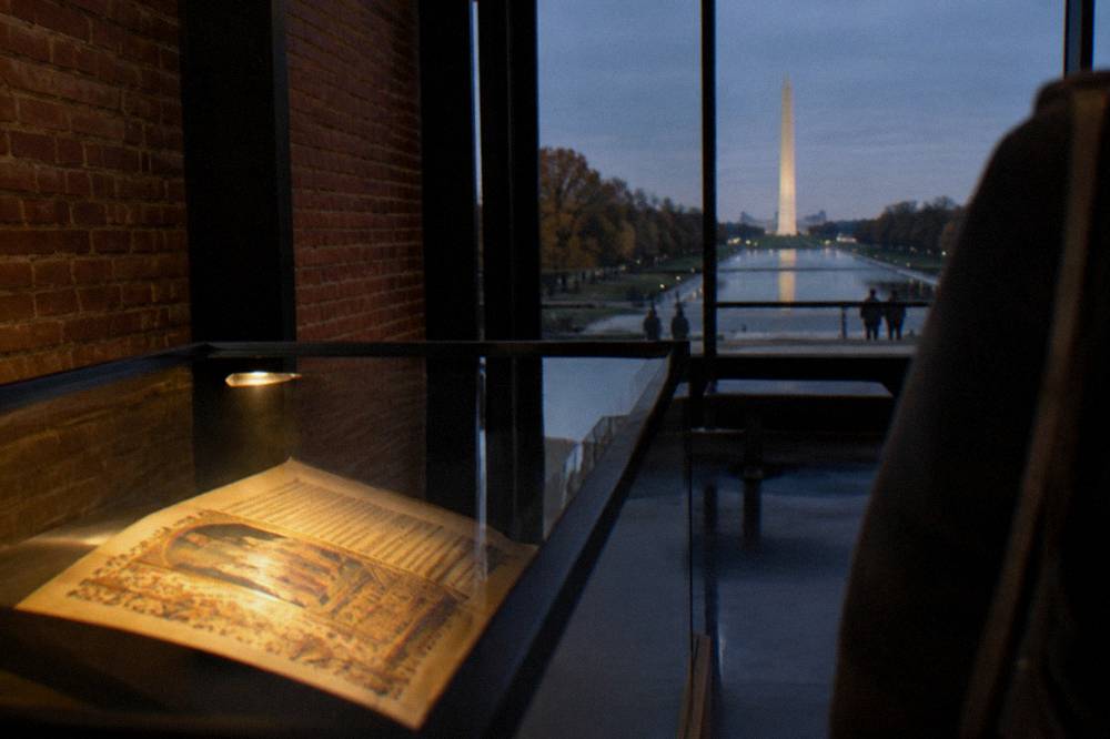 Ancient manuscript exhibit case with illuminated pages under display lighting