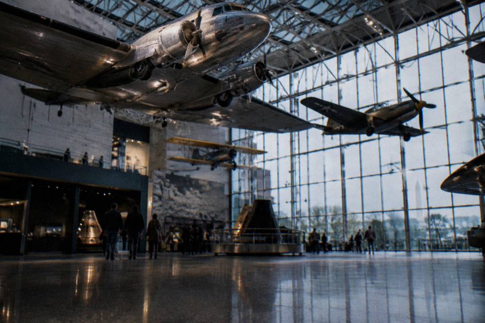 Visitors gathered around historic aircraft suspended from a museum gallery ceiling