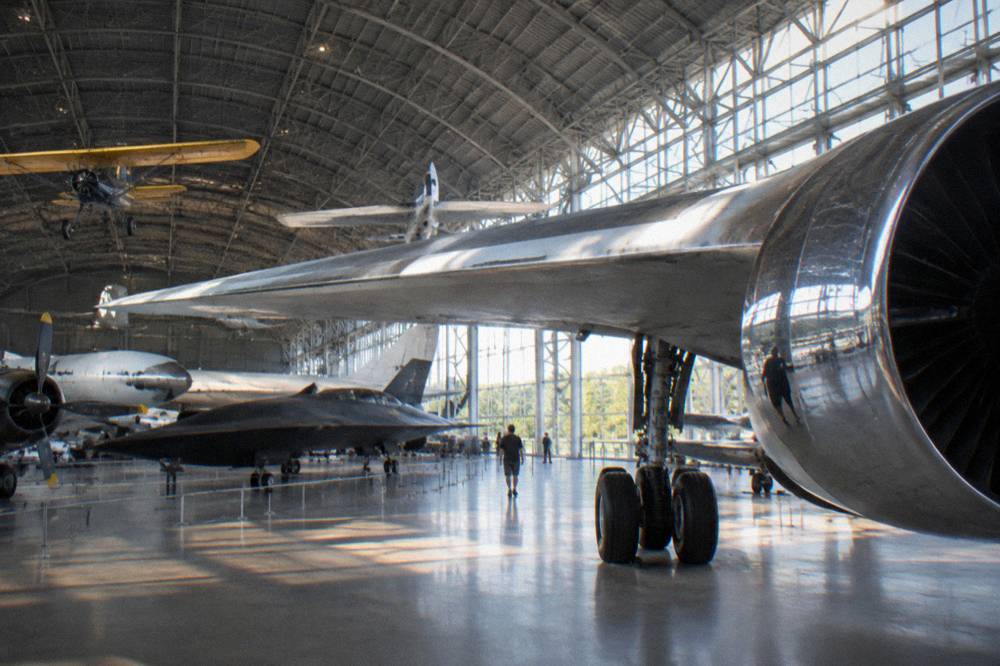 A large aviation hangar with historic aircraft parked across an open floor under a curved ceiling