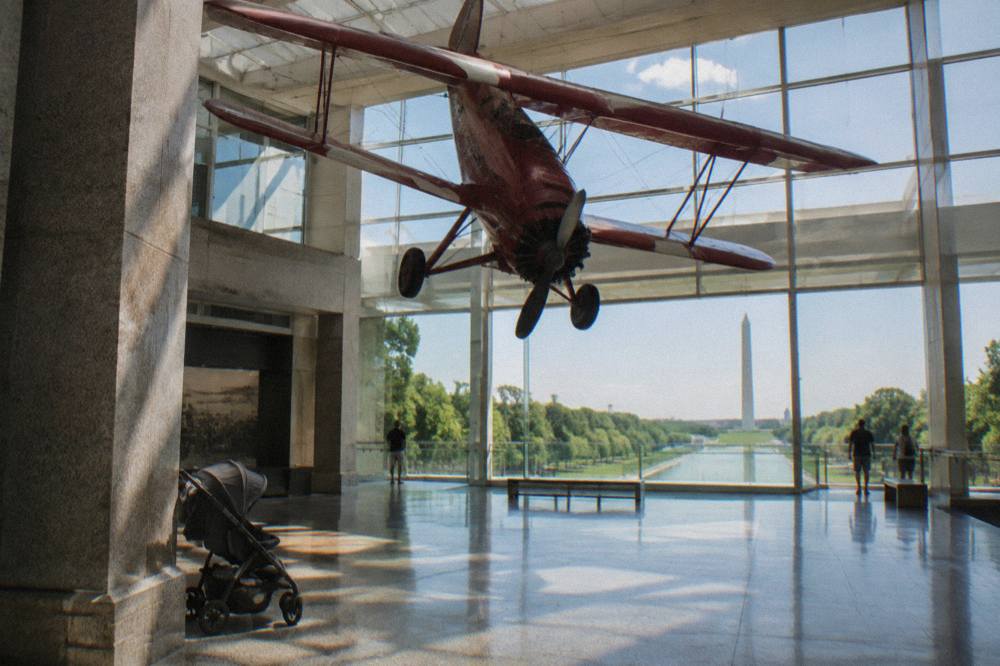 Sunlit museum gallery with a vintage mail plane suspended above the exhibit floor