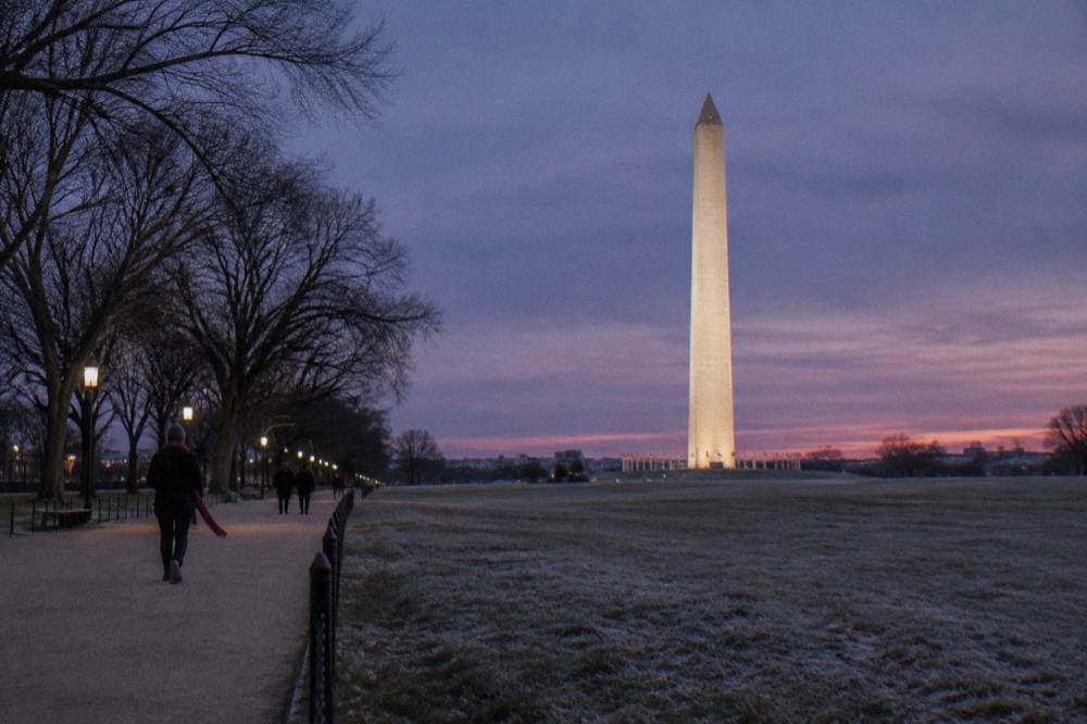 Illuminated memorial column and surrounding Mall landscape at dusk in Washington DC