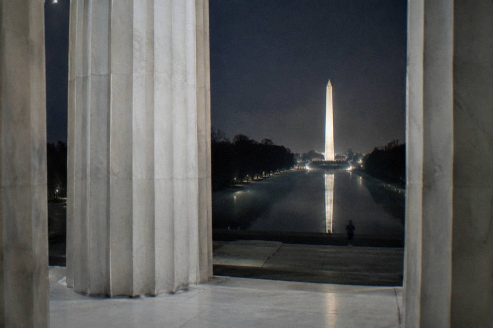 Lincoln Memorial glowing under floodlights beside a still reflecting pool at night