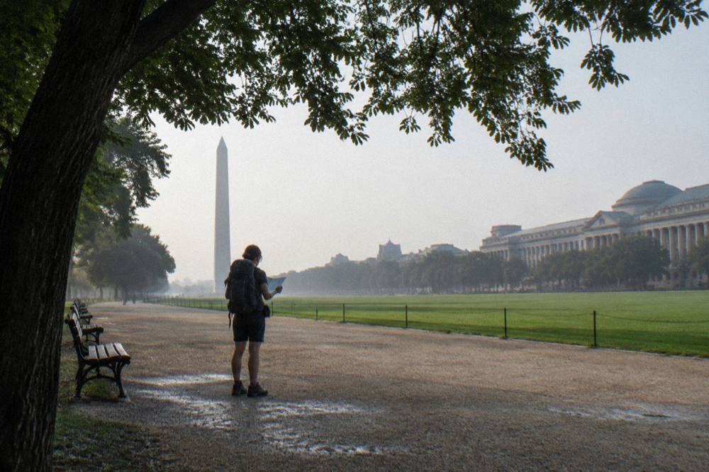 Visitor with a backpack consulting a map beside a museum-lined promenade in morning light