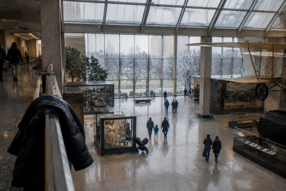 Interior of a bright museum gallery with high windows and families viewing exhibits