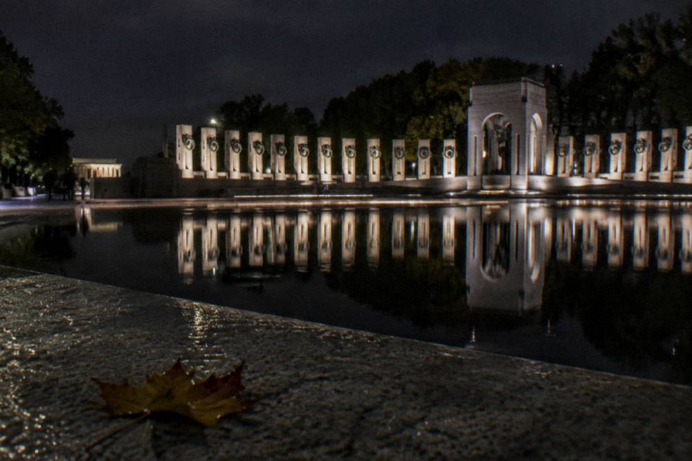 Illuminated memorial columns reflected in water at night on the National Mall