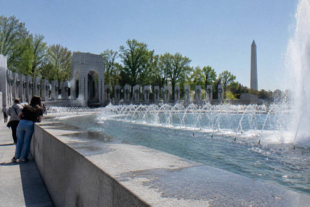 The World War II Memorial fountain and granite columns under a clear afternoon sky
