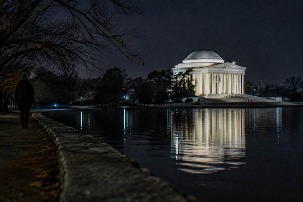 Illuminated memorial columns and reflecting pool seen at night under floodlights