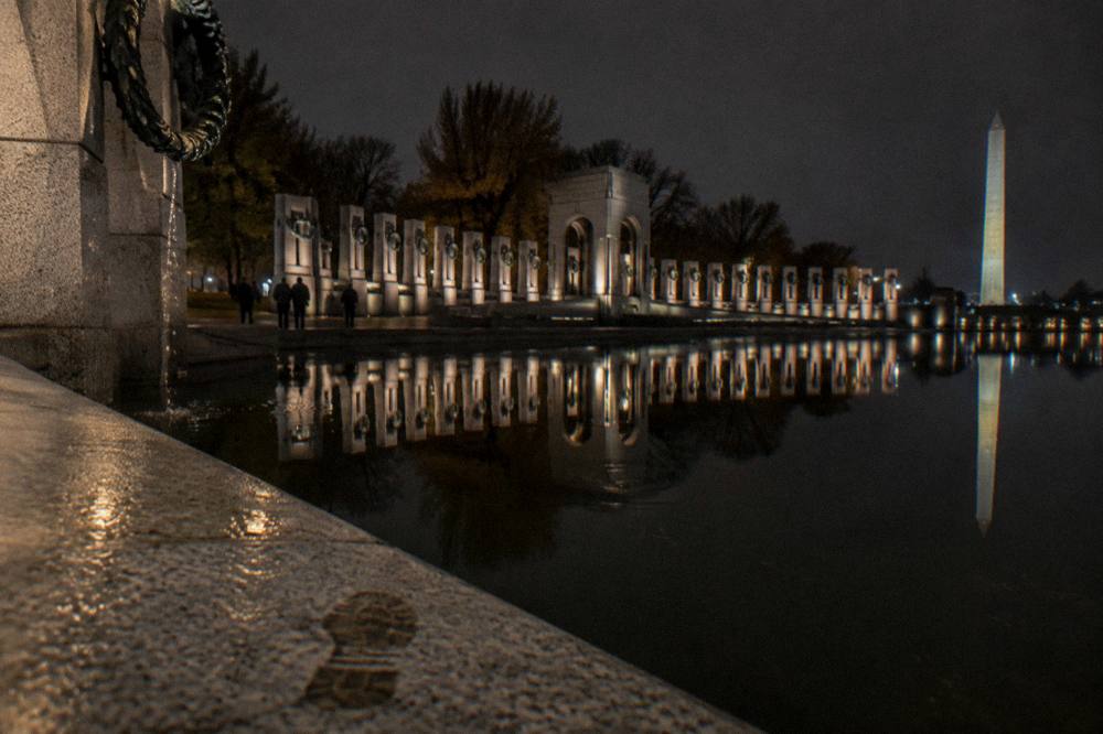 Illuminated memorial columns reflected in water after dark on the National Mall