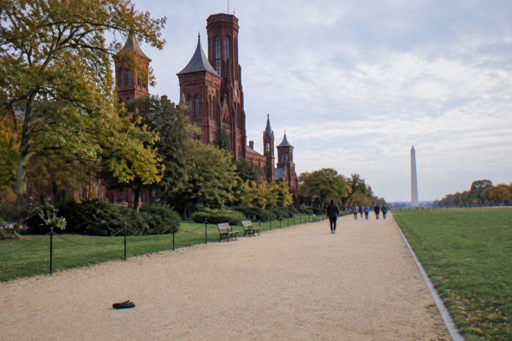 Wide path beside the Smithsonian castle building with museum visitors' distance view of the Mall